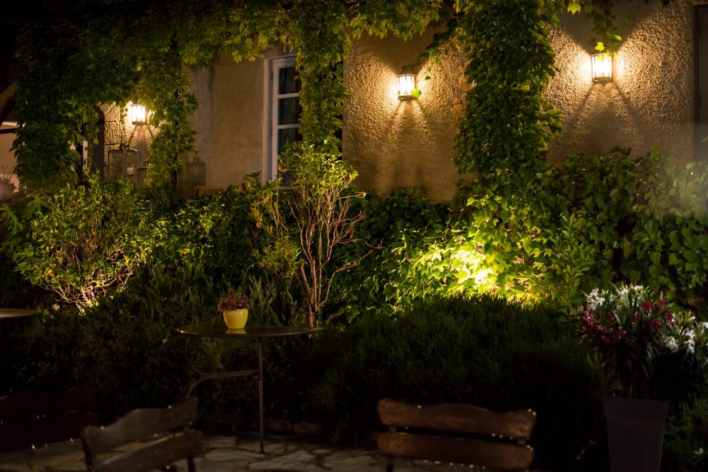 Building wall and garden lit by wall lights and uplights at night